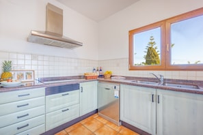 Eine Küche mit weißen Schränken, einem Edelstahl-Geschirrspüler und einem Fenster mit Blick auf einen Baum.