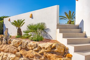 A modern building with a white exterior, a stone retaining wall, and a staircase leading to the entrance. - Villa Altamira - Plus (Calpe)