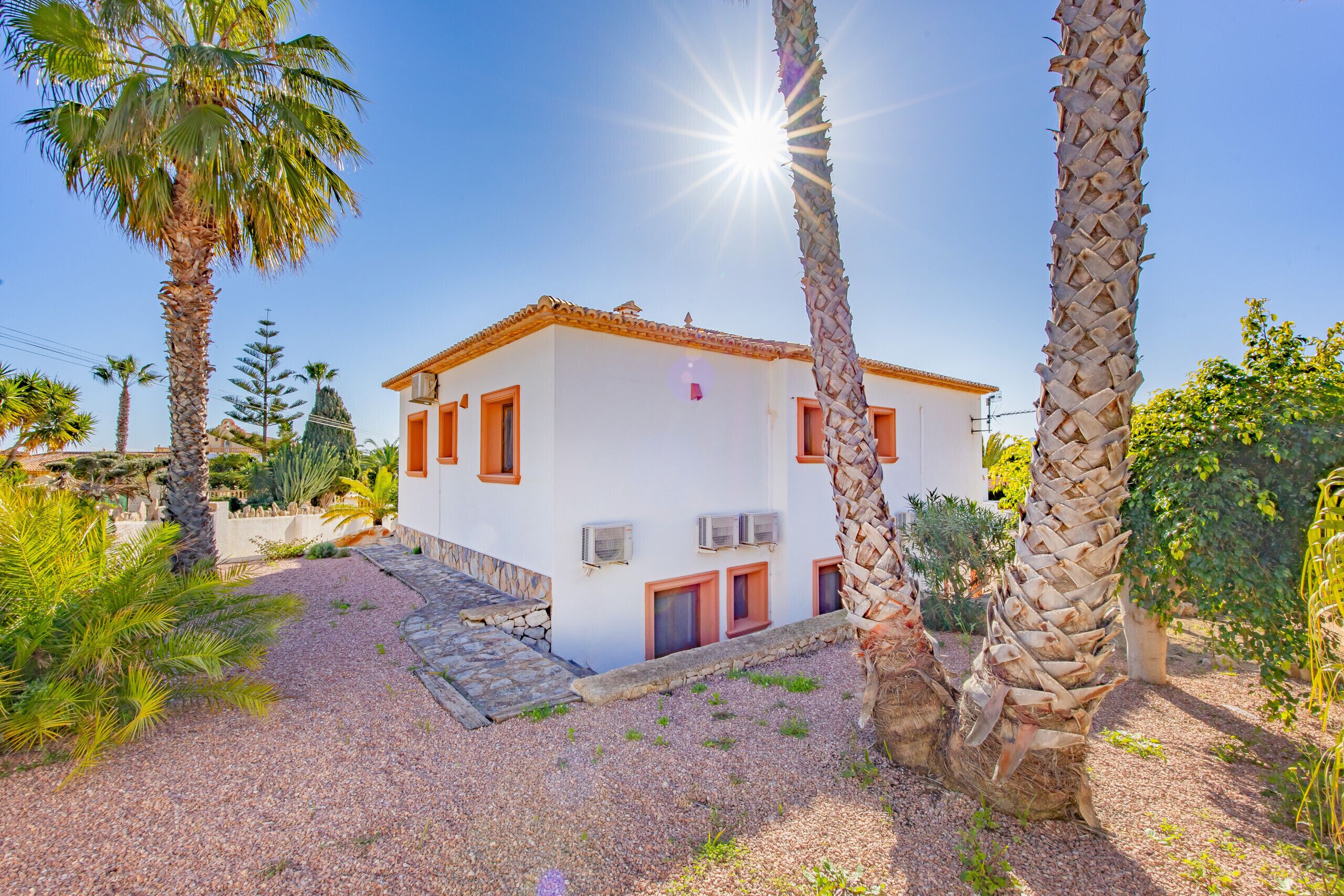 A white building with red accents, surrounded by palm trees and gravel paths.