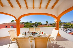 A terrace with a table set for a meal, surrounded by chairs, and a view of the city and mountains. - Villa Altamira - Plus (Calpe)