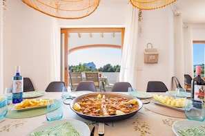 A dining table set with seafood paella, wine glasses, and plates, overlooking a scenic view. - Villa Altamira - Plus (Calpe)