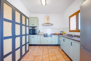 A kitchen with light blue cabinets, a stainless steel range hood, and a tiled floor. - Villa Altamira - Plus (Calpe)