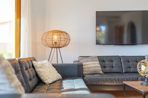 Ein modernes Wohnzimmer mit einer Ledersofa, einem großen Flachbildfernseher an der Wand und einer ungewöhnlichen, kugelförmigen Stehlampe.