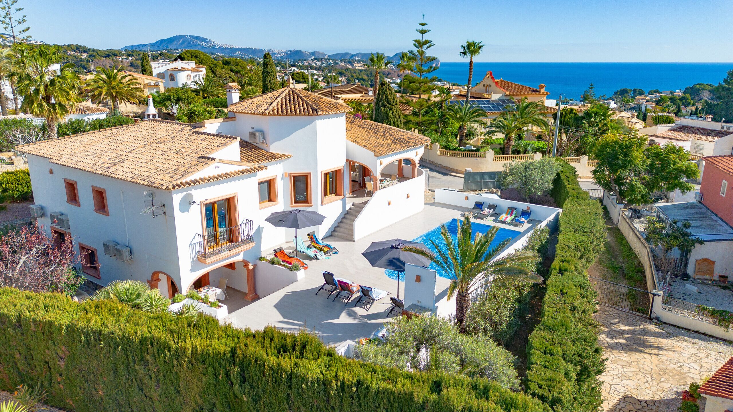 A Mediterranean-style villa with a swimming pool, multiple balconies, and a view of the sea.