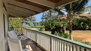 Un espace extérieur aménagé, abrité et doté de chaises et d’une table blanches, entouré d’une rambarde blanche, qui offre une vue sur un jardin paysager avec des palmiers et sur un bâtiment situé au loin.