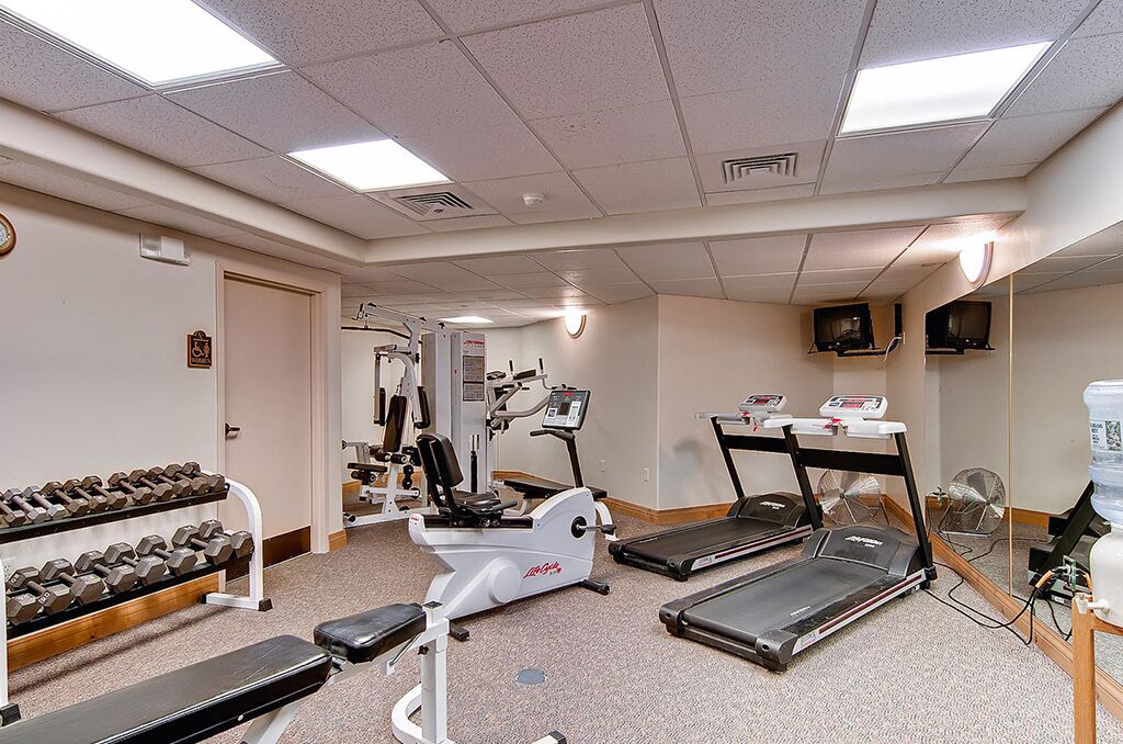 Une salle de sport équipée de tapis de course, d’un vélo elliptique et d’un banc de musculation.