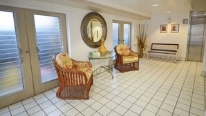 A spacious room with a tiled floor, two wicker chairs with floral upholstery, a round mirror, and a bench. - Sea Shore 41 Private Studio in Waikiki, 1 Block to Beach (Honolulu)