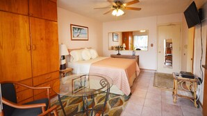 A bedroom with a bed, a glass table, a chair, a wardrobe, a ceiling fan, a television, and a door leading to another room. - Sea Shore 41 Private Studio in Waikiki, 1 Block to Beach (Honolulu)