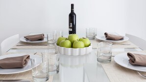 A dining table set with plates, glasses, a bowl of green apples, and a bottle of wine. - Blanca 1 - Habitat Apartments (Barcelona)