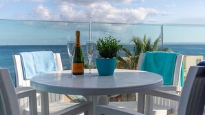 A round table with a bottle of champagne and a glass, surrounded by white chairs with blue towels.