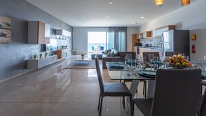 A modern kitchen with built-in appliances, a dining area with a glass table, and a living space with a sofa and a view of the outdoors.