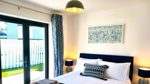 Hotelkamer met een bed, twee bedlampen, een schilderij en uitzicht op een witte schutting door een glazen deur.