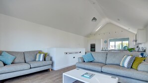 Een moderne woonkamer met twee grijze banken, een witte salontafel en een keuken op de achtergrond.