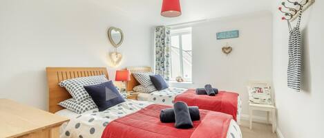 A bedroom with two beds, a wooden nightstand, a red lamp, a heart-shaped mirror, and a view of the outside.
