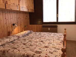 A wooden-paneled room with a bed, a window, and a wall-mounted heater.