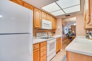 Una cucina con mobili in legno, un frigorifero bianco, un forno a microonde, un forno e un lavello.