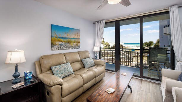 Un soggiorno con un divano beige, un tavolino in legno, un comodino scuro con una lampada e un quadro raffigurante una spiaggia.