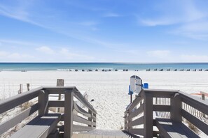 Une plage avec une promenade en bois menant à l’eau, un panneau indiquant une zone où la baignade est interdite, et un poste de surveillance pour les sauveteurs.