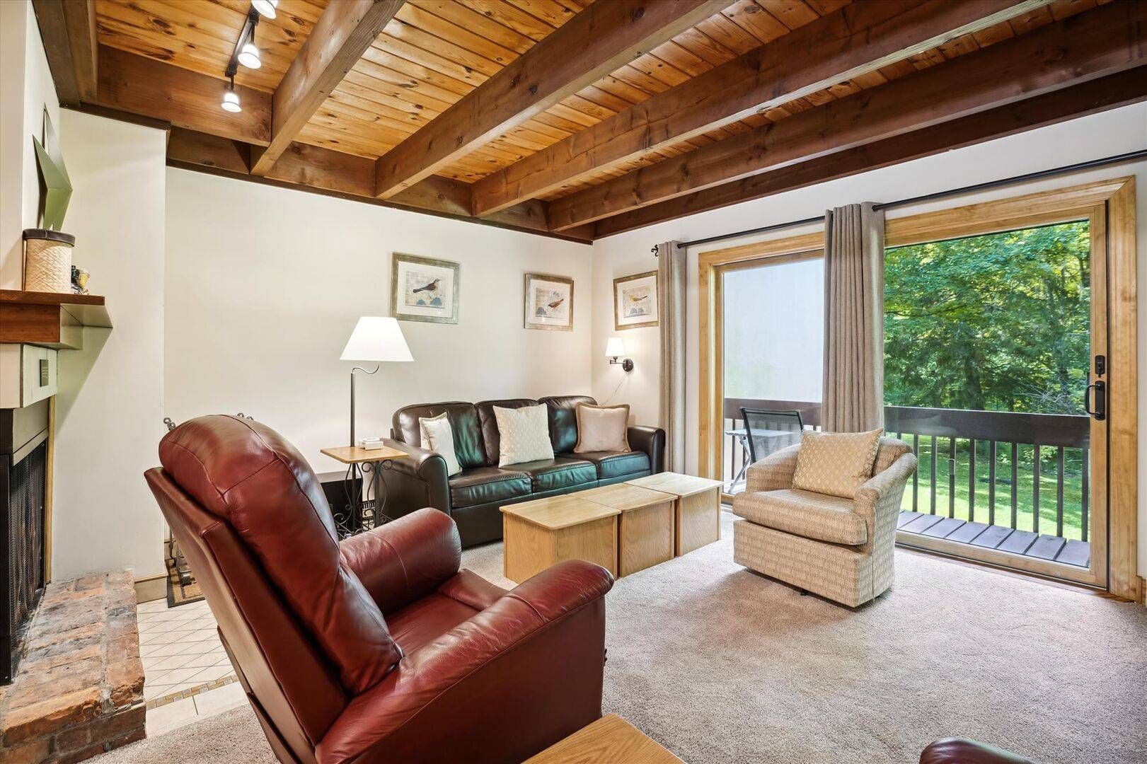 A cozy living room with a fireplace, a sofa, a chair, and a balcony with a view of greenery.