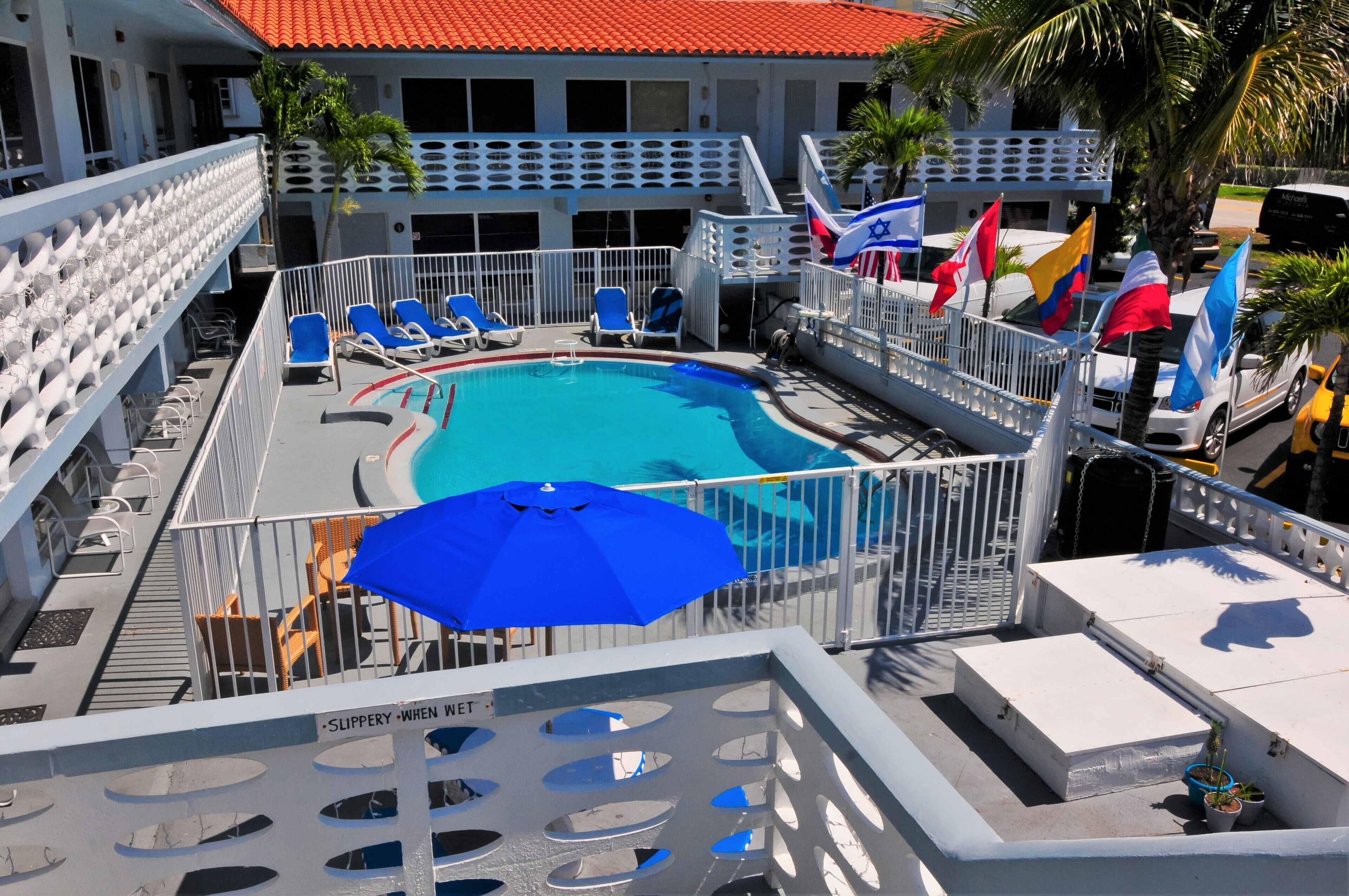Un espace piscine avec des chaises longues, un parasol bleu et des drapeaux.
