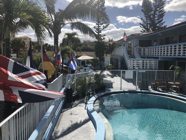 A pool area with flags, a fenced deck, and a building with a unique architectural design.