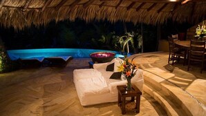 An outdoor lounge area with a thatched roof, a pool, and a dining setup. - Villa Encantada at Pacific Vacation | StayPV Oceanfront Luxury with Staff (Zihuatanejo)