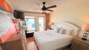 A hotel room with a bed, a television, a ceiling fan, and a view of the beach. - Beachfront 3BR | Stunning Views&Dual Living Areas (Destin)
