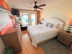 Une chambre d’hôtel avec un lit, une télévision, un ventilateur de plafond et une vue sur la plage.