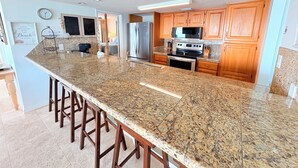A spacious kitchen with granite countertops, wooden cabinets, stainless steel appliances, and a large island with bar stools. - Beachfront 3BR | Stunning Views&Dual Living Areas (Destin)
