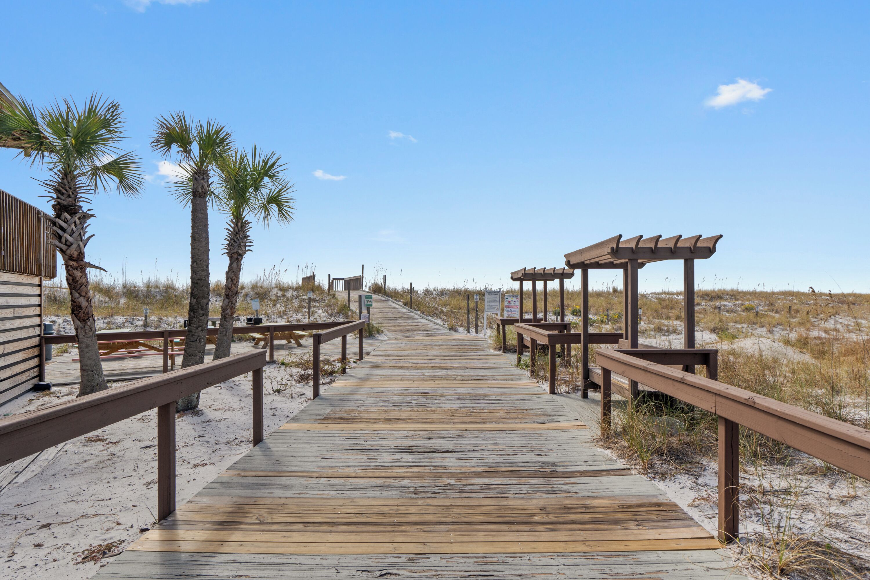 A wooden boardwalk leading to a beach area with palm trees and a wooden structure.