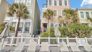 A row of beachside condominiums with balconies, palm trees, and lounge chairs.