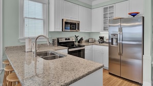 A modern kitchen with white cabinets, a stainless steel refrigerator, a microwave, a stove, and a sink.