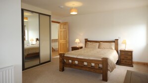Une chambre à coucher avec un lit en bois, deux tables de chevet avec des lampes, un grand miroir et une porte en bois.