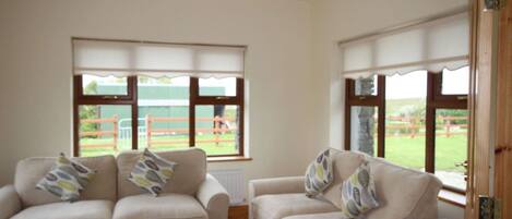 A room with two beige sofas, a glass coffee table, and large windows with blinds.