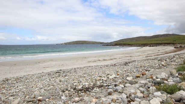 Une plage de galets offrant une vue sur la mer et les collines lointaines.