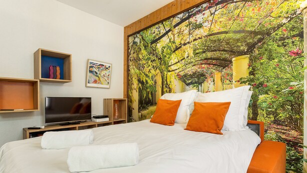 Une chambre d’hôtel avec un grand lit, un téléviseur à écran plat, un tableau et une fresque représentant un jardin.