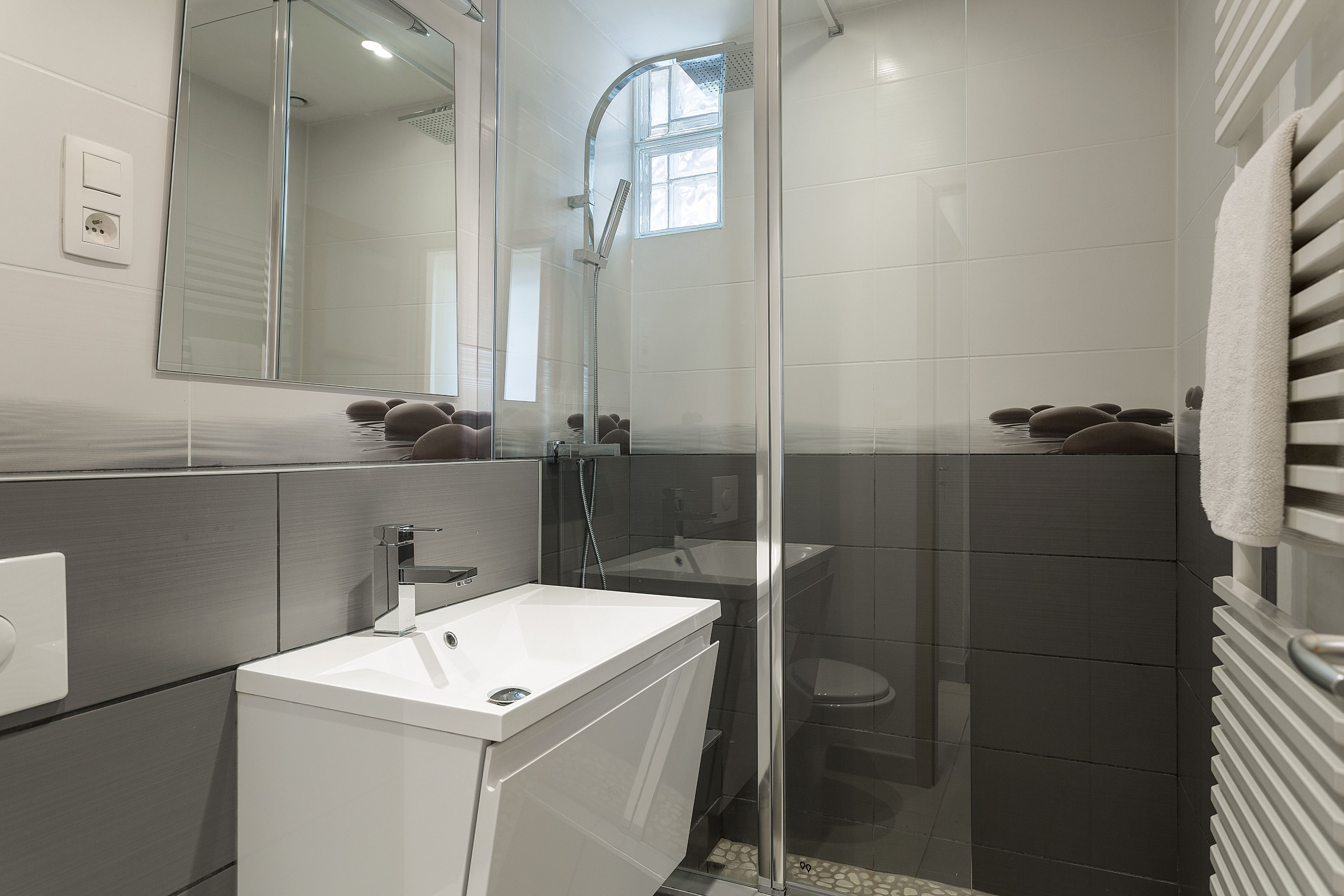 A modern bathroom with a glass-enclosed shower, a white sink, and a towel rack.