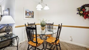 Een eetgedeelte met een ronde tafel, vier stoelen, een vaas met bloemen, een schilderij aan de muur en een kroonluchter.