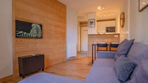 A modern living room with a grey sofa, wooden panel walls, a painting of a zebra, a small cabinet, and a kitchen in the background. - A central, one bedroom apartment, perfect for a couple or small group. (Chamonix-Mont-Blanc)