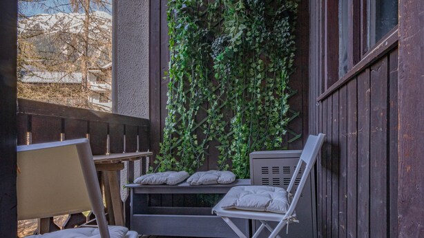 A cozy outdoor seating area with a wooden bench and a folding chair, a small table, and a wall covered in green ivy. - A central, one bedroom apartment, perfect for a couple or small group. (Chamonix-Mont-Blanc)