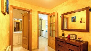 Een hal met houten deuren die leiden naar een badkamer en een keuken. Er staat een houten dressoir met lades en een spiegel erboven.