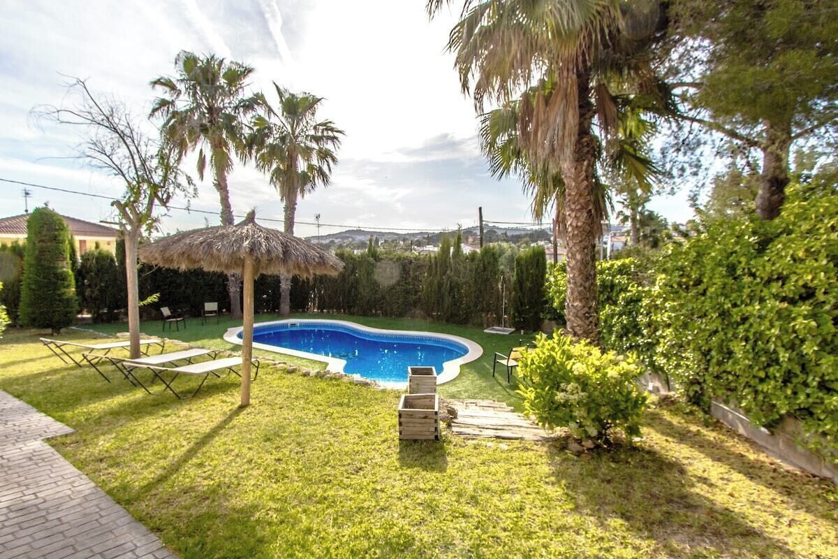 Ein Garten mit Swimmingpool, Palmen und einem Reetdachschirm.