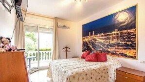 Een slaapkamer met een bed, een schilderij van een nachthemel, een houten dressoir en een balkon met gordijnen.