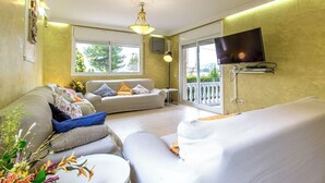 Een moderne slaapkamer met een sofa, een bed, een televisie en een balkon met uitzicht op groen.