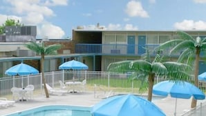 A swimming pool with a white fence, blue umbrellas, and lounge chairs.