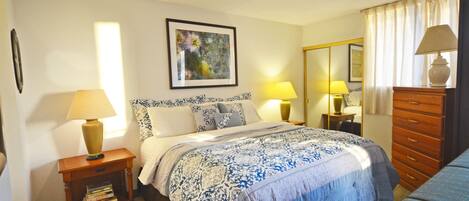 A bedroom with a bed, bedside lamps, a dresser, a mirror, and a framed picture on the wall.