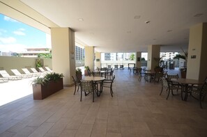 An indoor patio area with multiple tables and chairs, large windows, and potted plants.