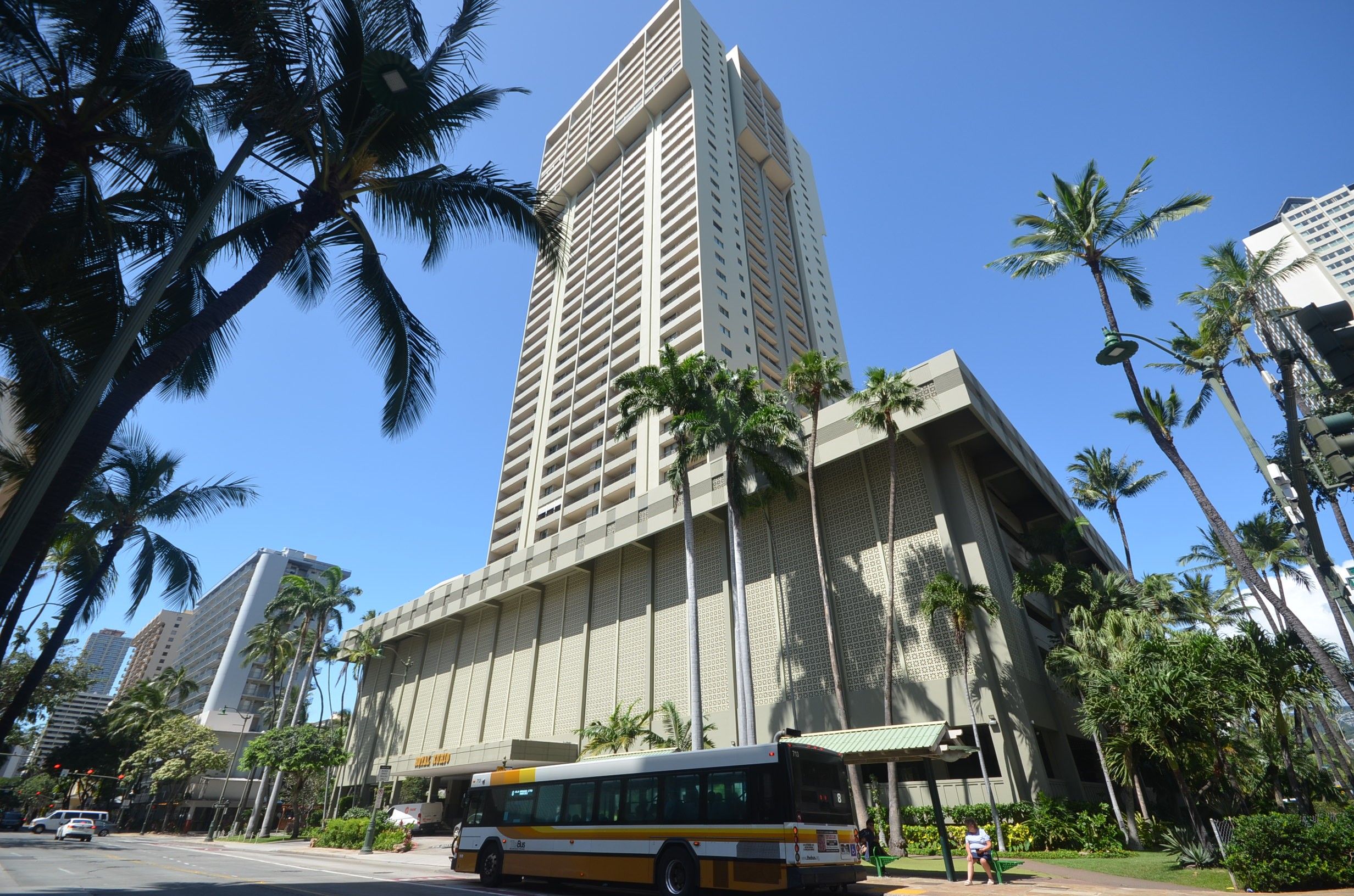 A tall building with a modern design, surrounded by palm trees and a clear blue sky.