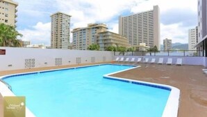 A rooftop swimming pool with lounge chairs, surrounded by high-rise buildings. - Royal Kuhio 1309 with King Bed, FREE Parking/WiFi, mins to BEACH! (Honolulu)