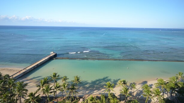 A beach with clear turquoise water, a pier extending into the sea, and palm trees lining the shore. - Royal Kuhio 1309 with King Bed, FREE Parking/WiFi, mins to BEACH! (Honolulu)